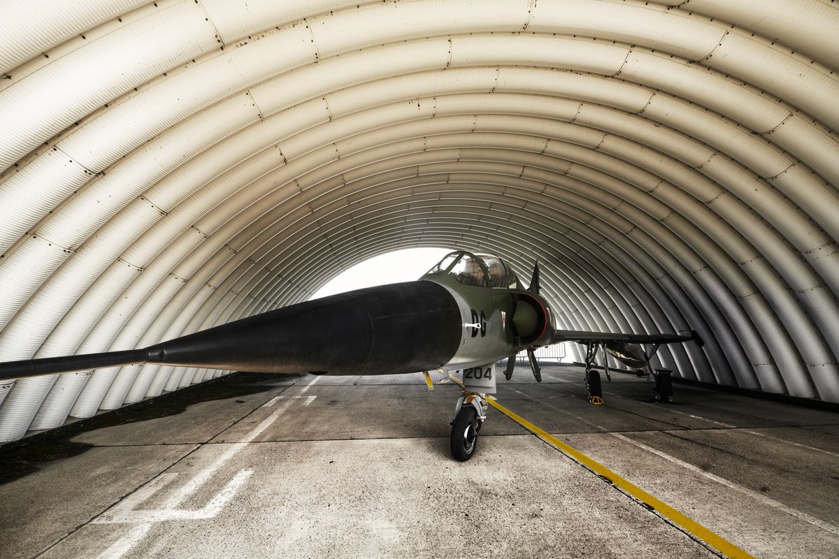 Military jet aircraft parked inside an arched hangar