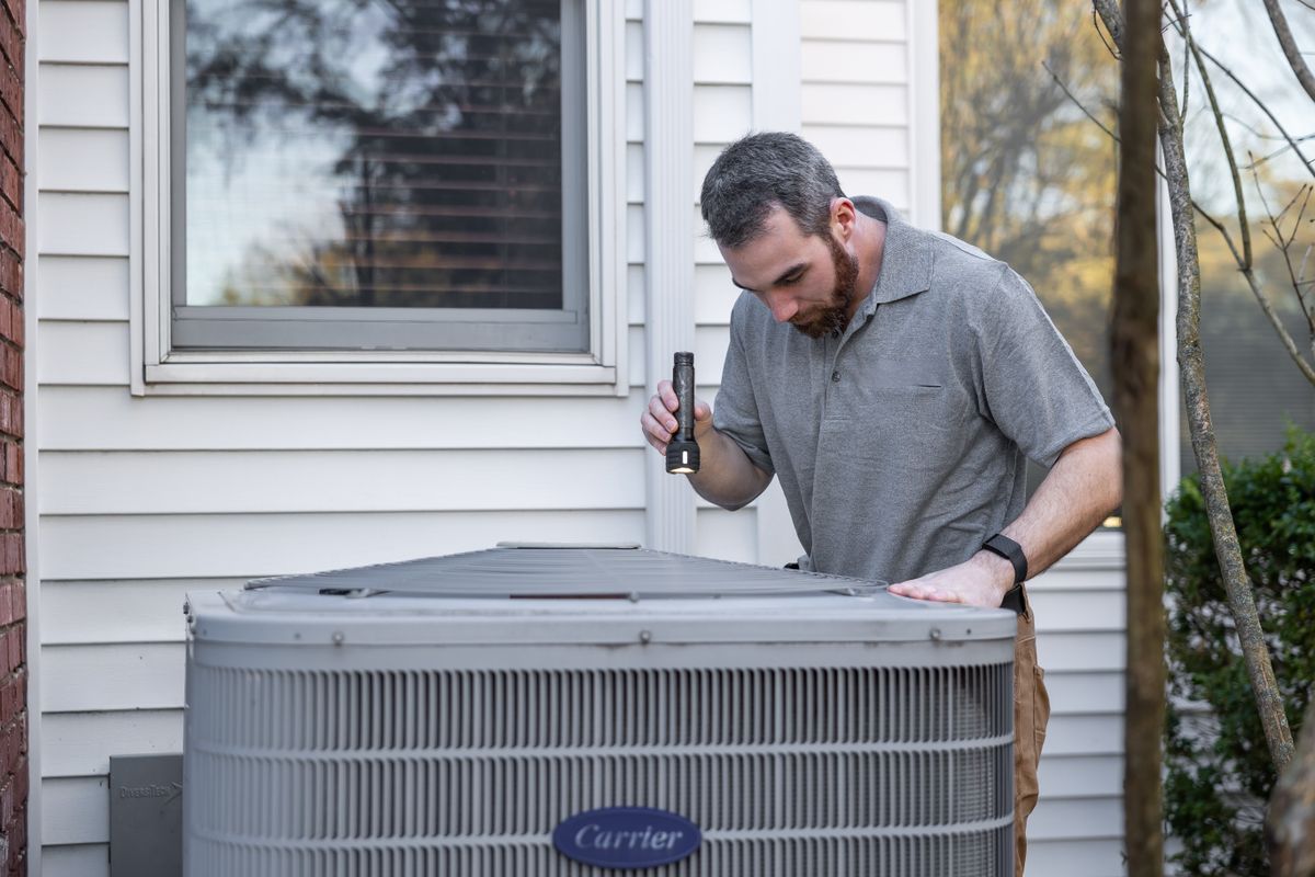 Field technician inspecting an outdoor HVAC unit with a flashlight